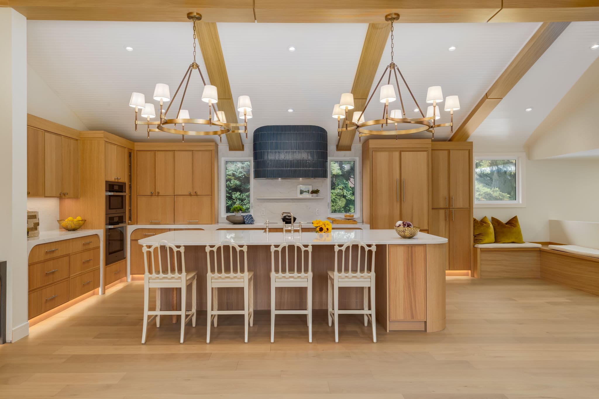 Symmetrical white oak kitchen with a curved island, vaulted ceiling, and twin chandeliers in the Varal Road renovation by Platinum Build Homes in Varsity, Calgary.