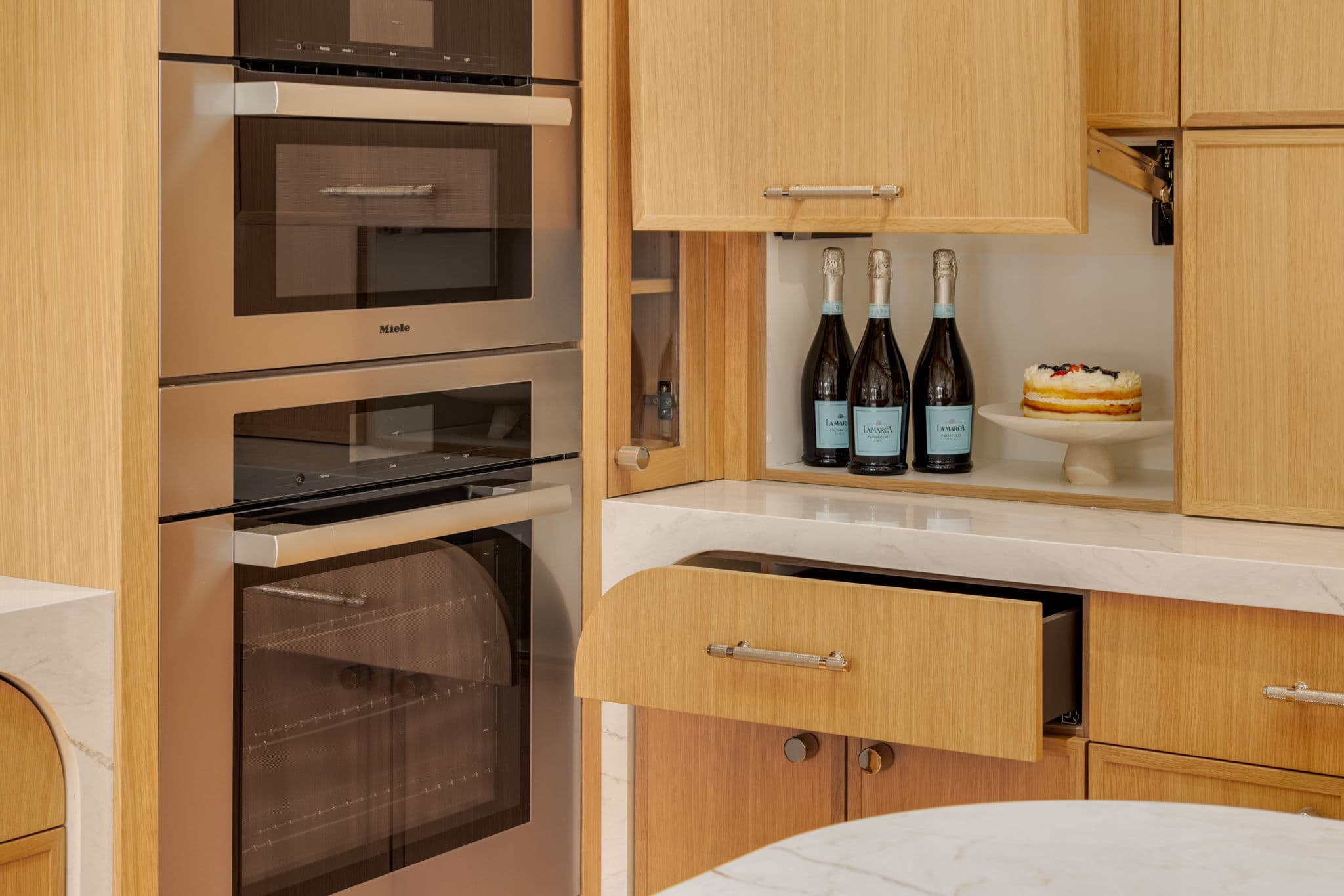 Built-in ovens and a concealed appliance garage within white oak cabinetry in the Varal Road renovation by Platinum Build Homes in Varsity, Calgary.