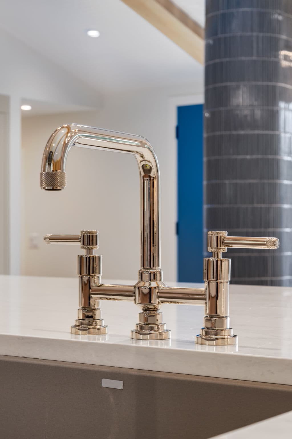 Polished nickel kitchen faucet with blue tile and quartz surfaces in the Varal Road renovation by Platinum Build Homes in Varsity, Calgary.
