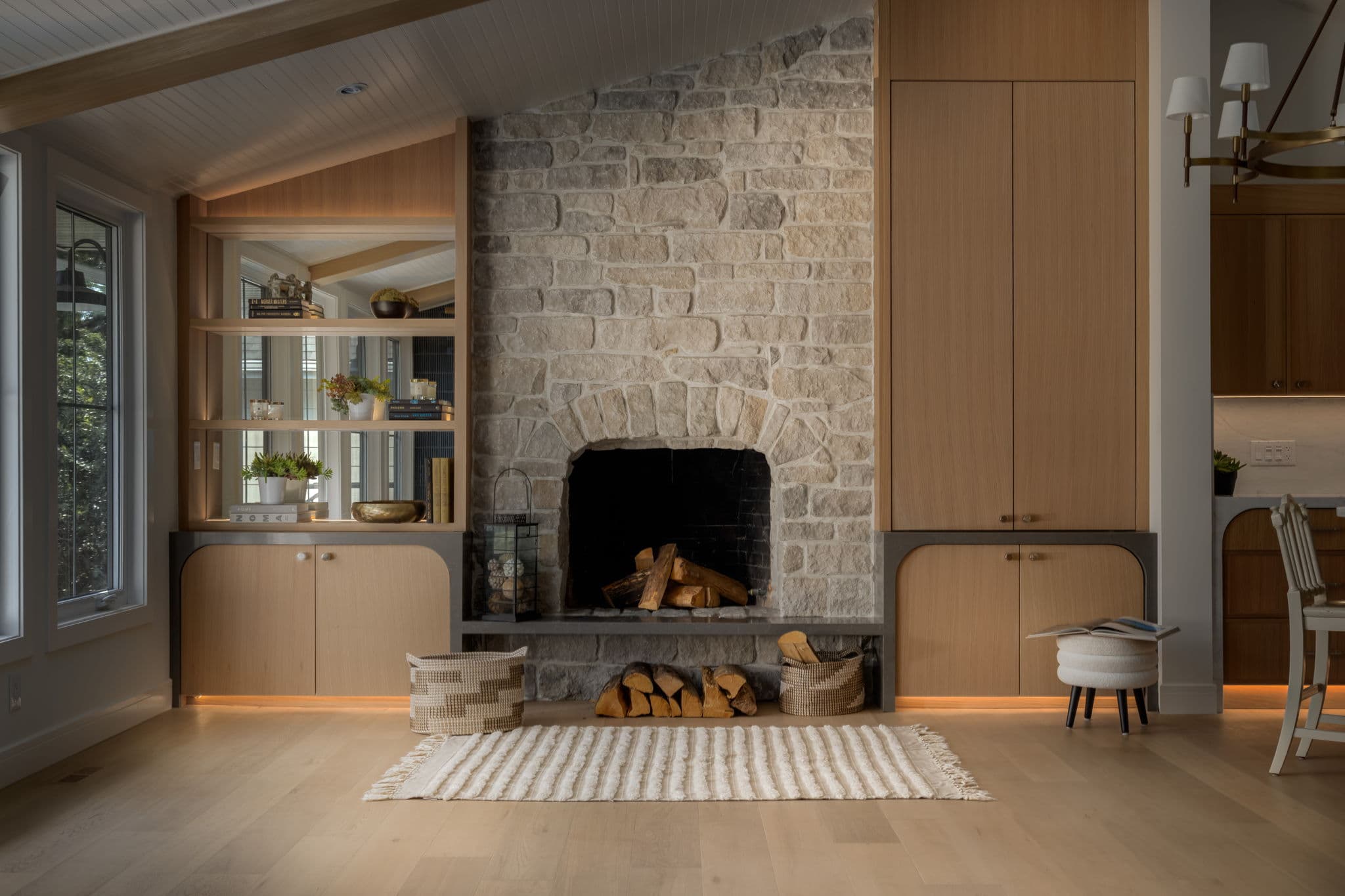 Tumbled limestone fireplace with white oak cabinetry and log storage in the Varal Road renovation by Platinum Build Homes in Varsity, Calgary.