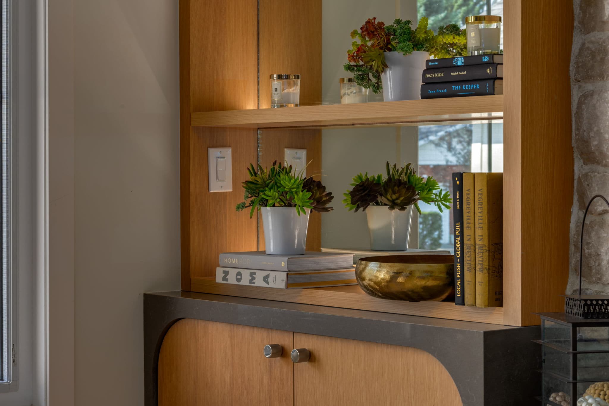 Custom white oak shelving and rounded cabinetry beside the limestone fireplace in the Varal Road renovation by Platinum Build Homes in Varsity, Calgary.