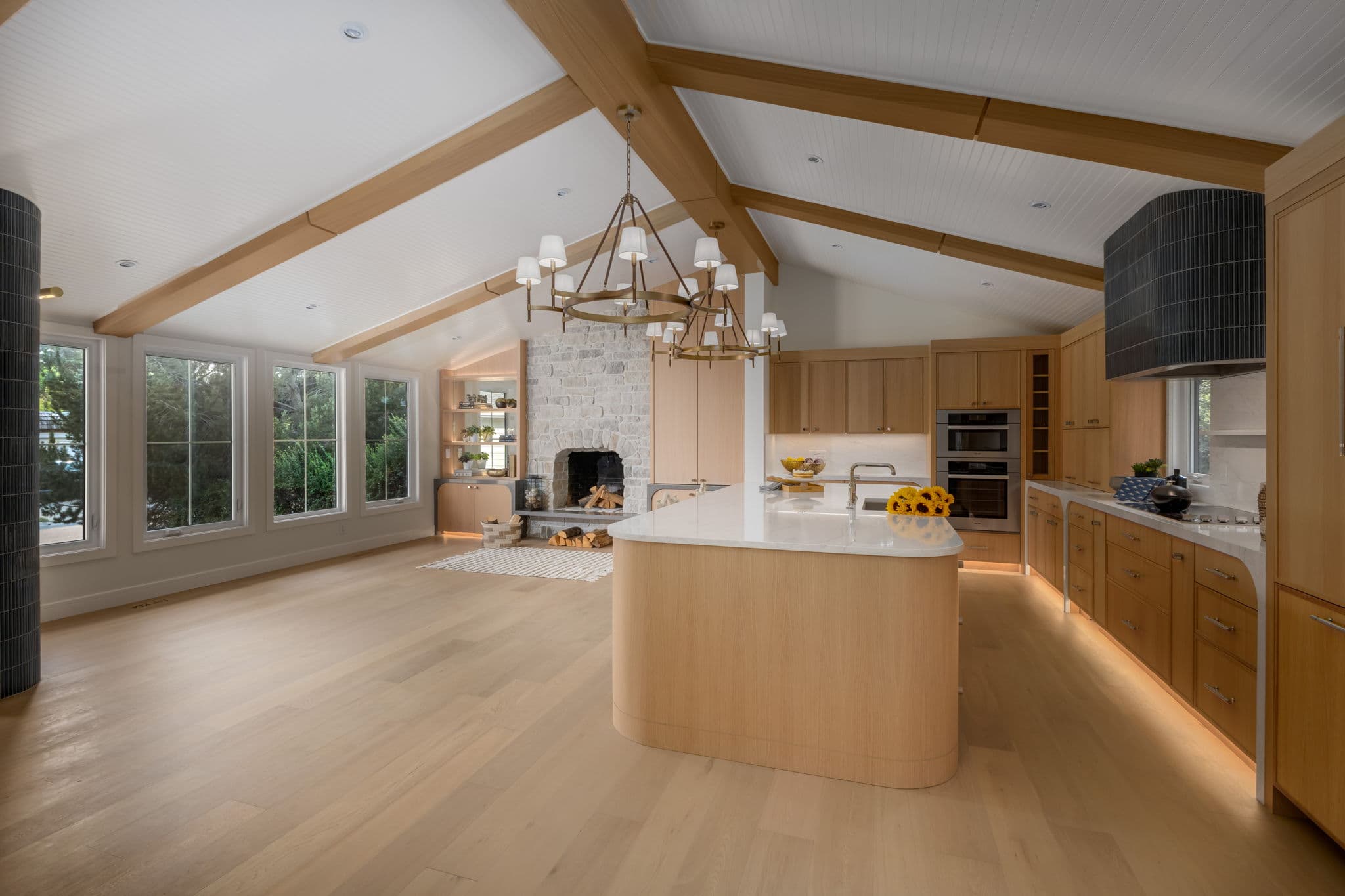 Wide view of the vaulted kitchen and living space with a curved island and limestone fireplace in the Varal Road renovation by Platinum Build Homes in Varsity, Calgary.