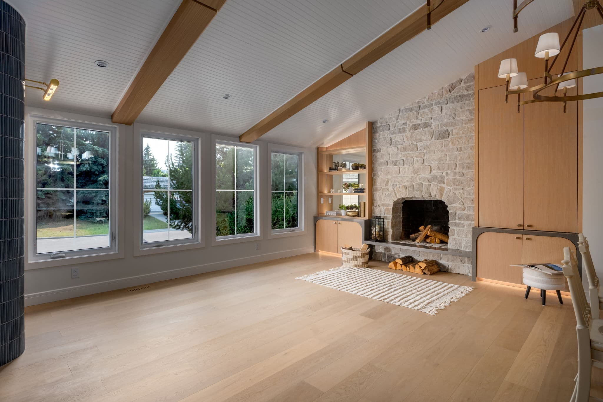 Living room with oak beams, white oak cabinetry, and a tumbled limestone fireplace in the Varal Road renovation by Platinum Build Homes in Varsity, Calgary.
