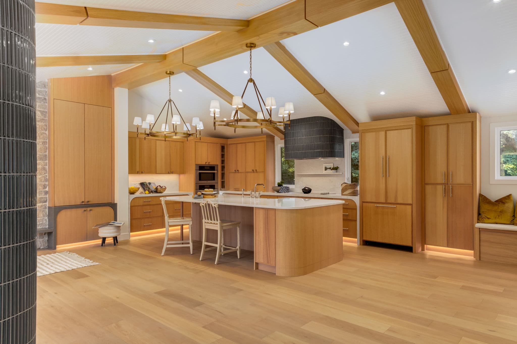 Vaulted kitchen with a curved white oak island and twin chandeliers in the Varal Road renovation by Platinum Build Homes in Varsity, Calgary.